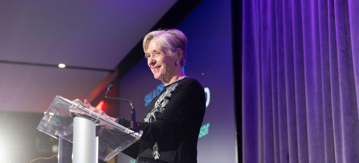 Dr. Manno speaks on stage behind a lectern. 