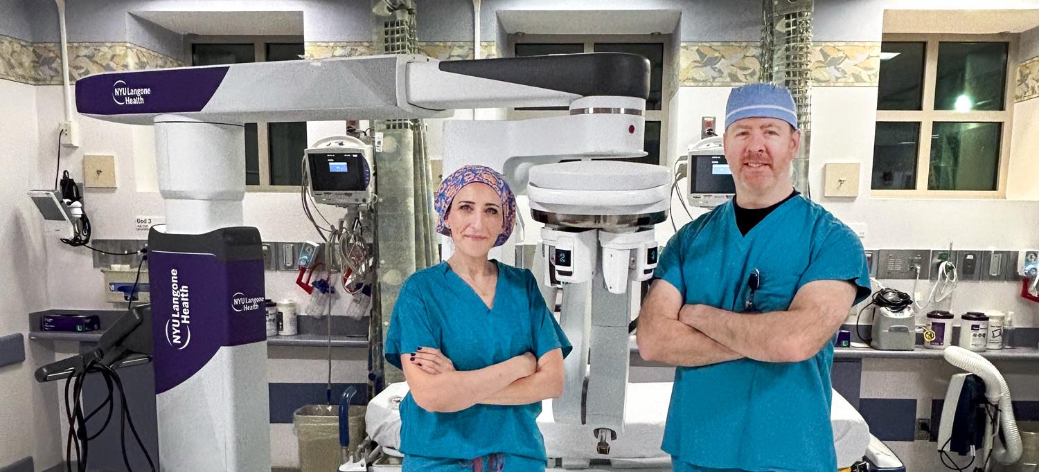 Dr. Martinez and Dr. Corcoran stand in front of robotic surgery equipment they use.