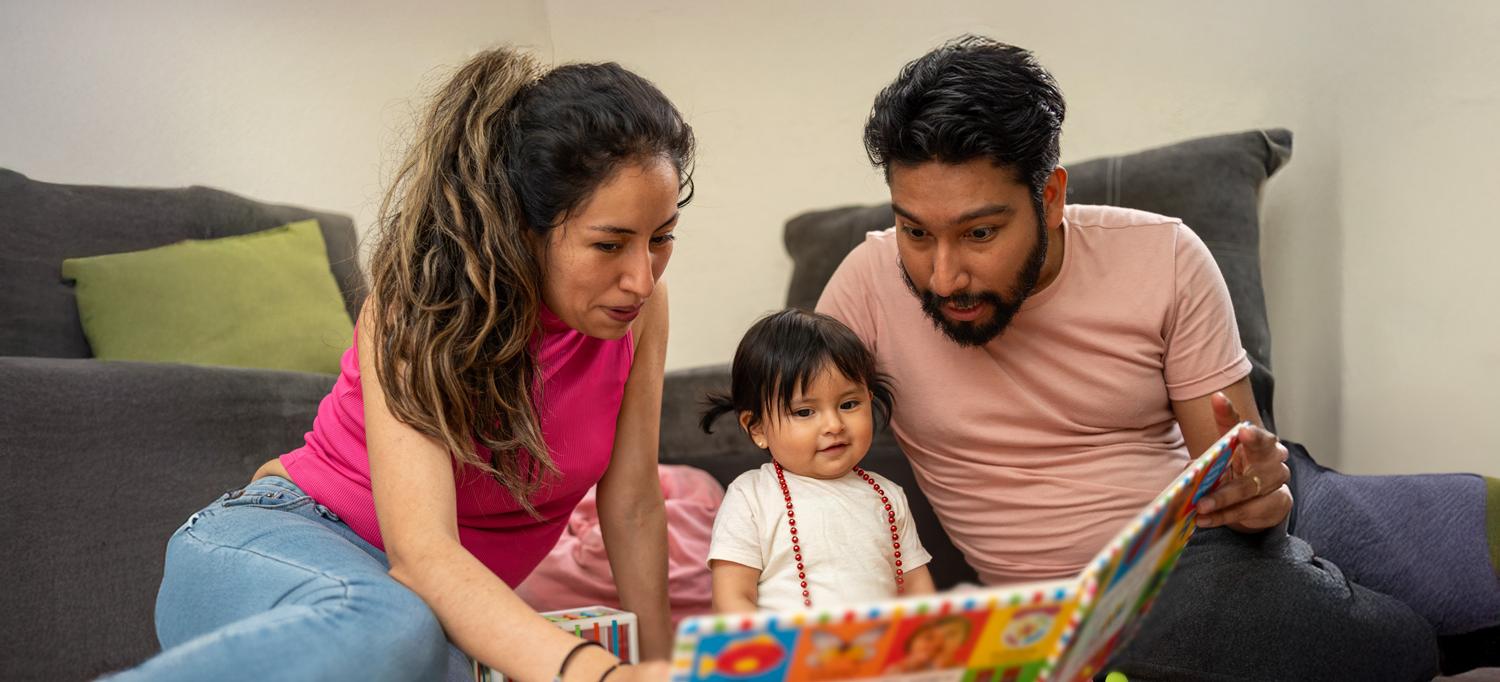 Young Hispanic parents reading a book to their child