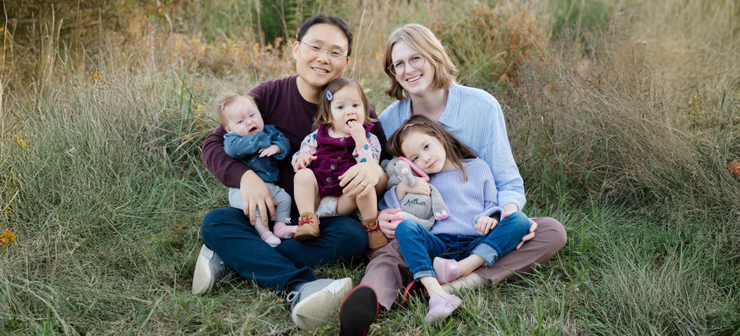 The family sits smiling, with grass in the background