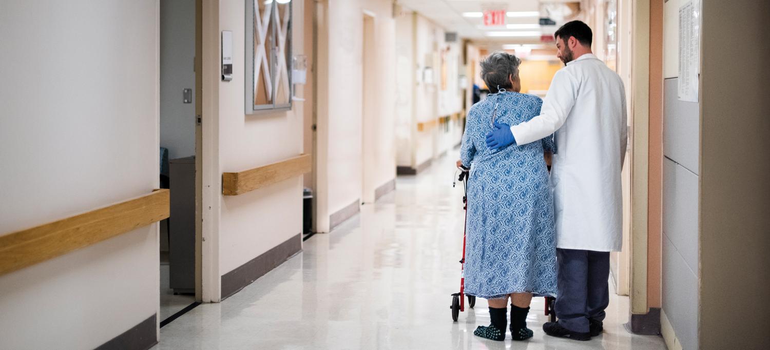 A doctor stands with his arm around a patient in a hospital hallway.