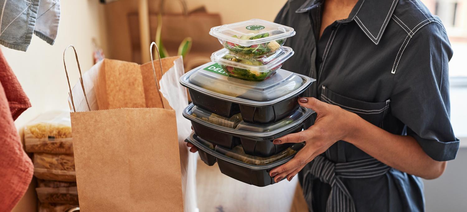 Woman carrying a stack of plastic containers filled with deli food 