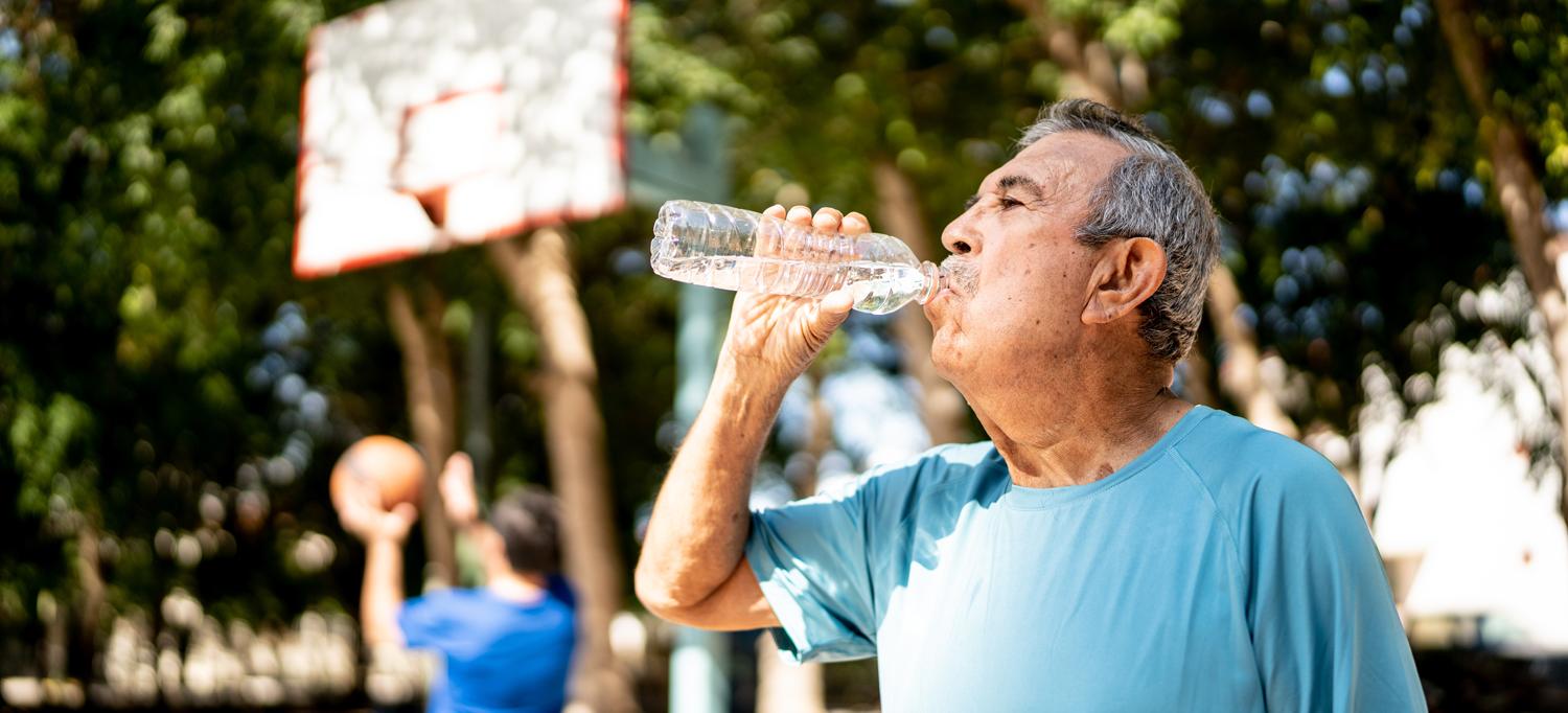 Older man drinking from a water bottle at the basketball court  