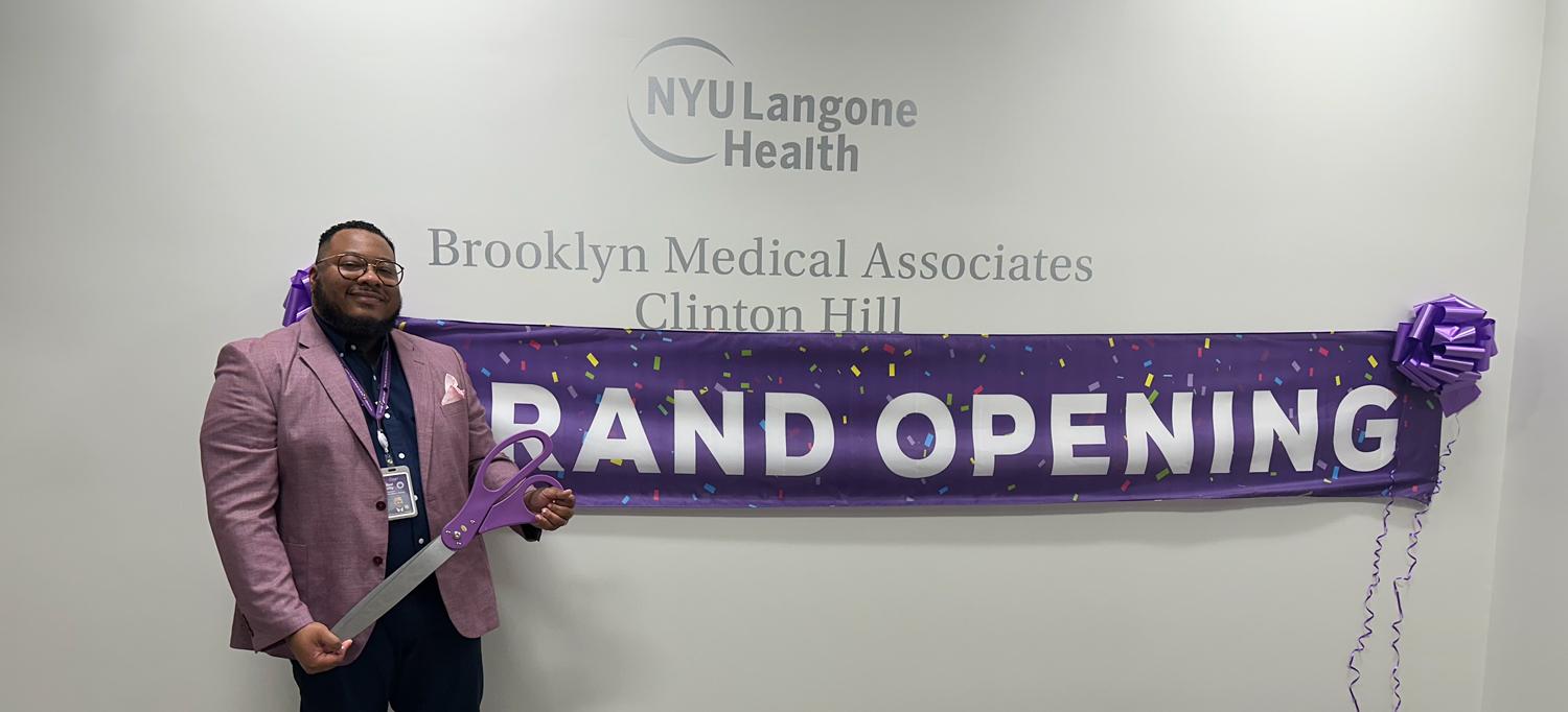 Man standing in front of a banner saying Grand Opening and a wall with “NYU Langone Brooklyn Medical Associates—Clinton Hill” on it. 