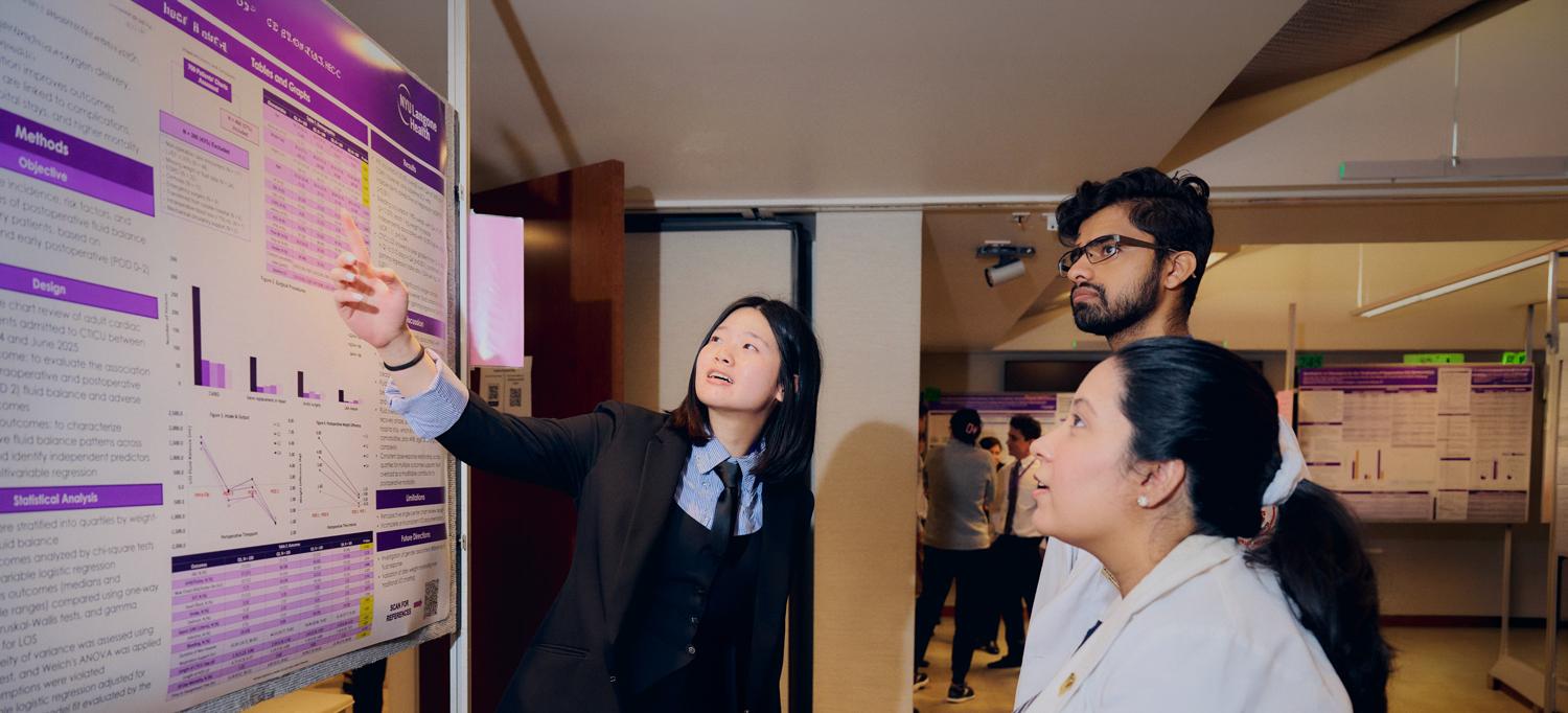 A researcher points to a wall chart while two others look on.