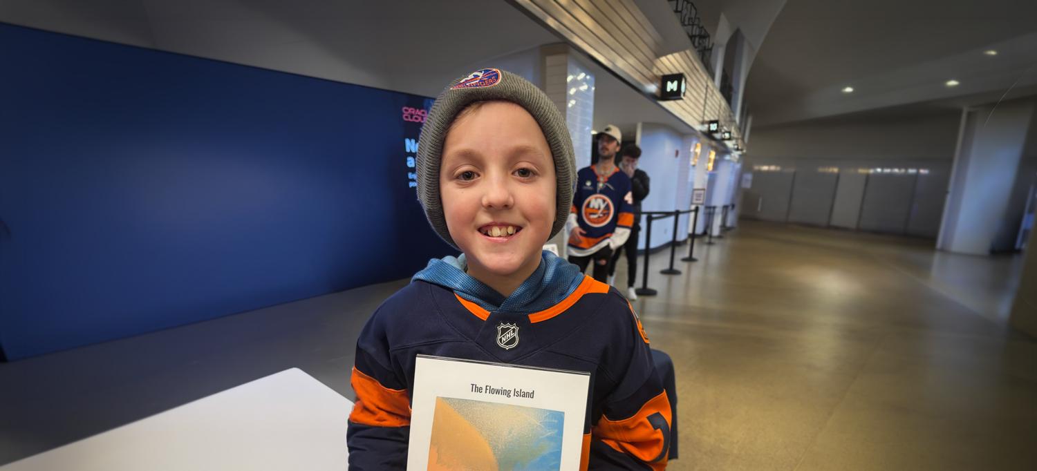 Logan stands in a hall holding a picture and text titled "The Floating Island."