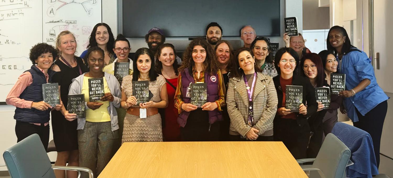 A group of NYU Langone employees stand smiling and holding copies of the book Pieces You'll Never Get Back, by Samina Ali.