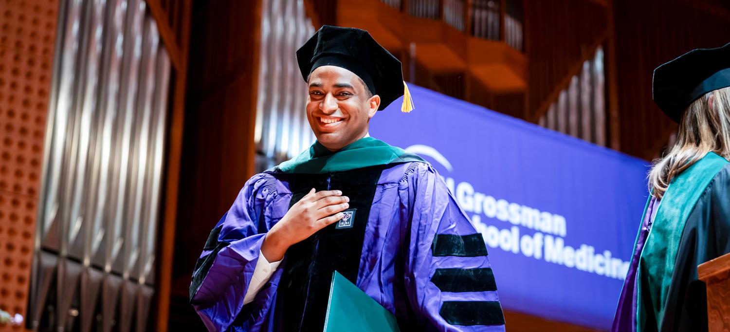 A medical school graduate walks across the stage with his diploma.