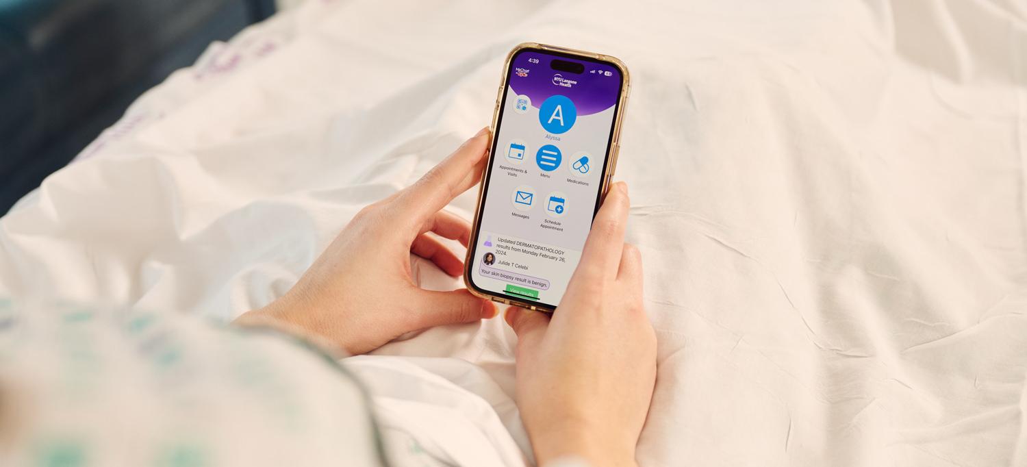 A person in bed holds a smartphone with an NYU Langone app open.