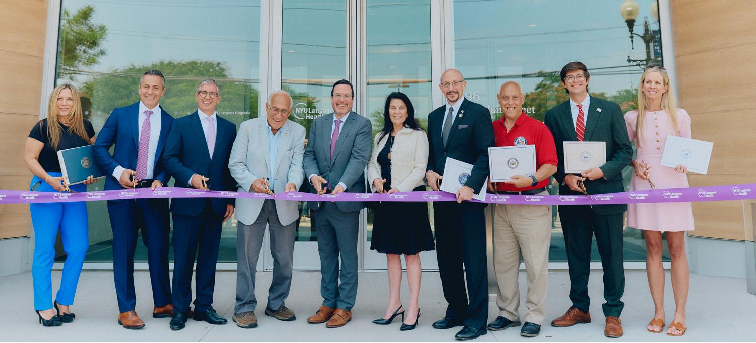 A group of smiling people prepare to cut the ribbon as part of the building’s official opening. 