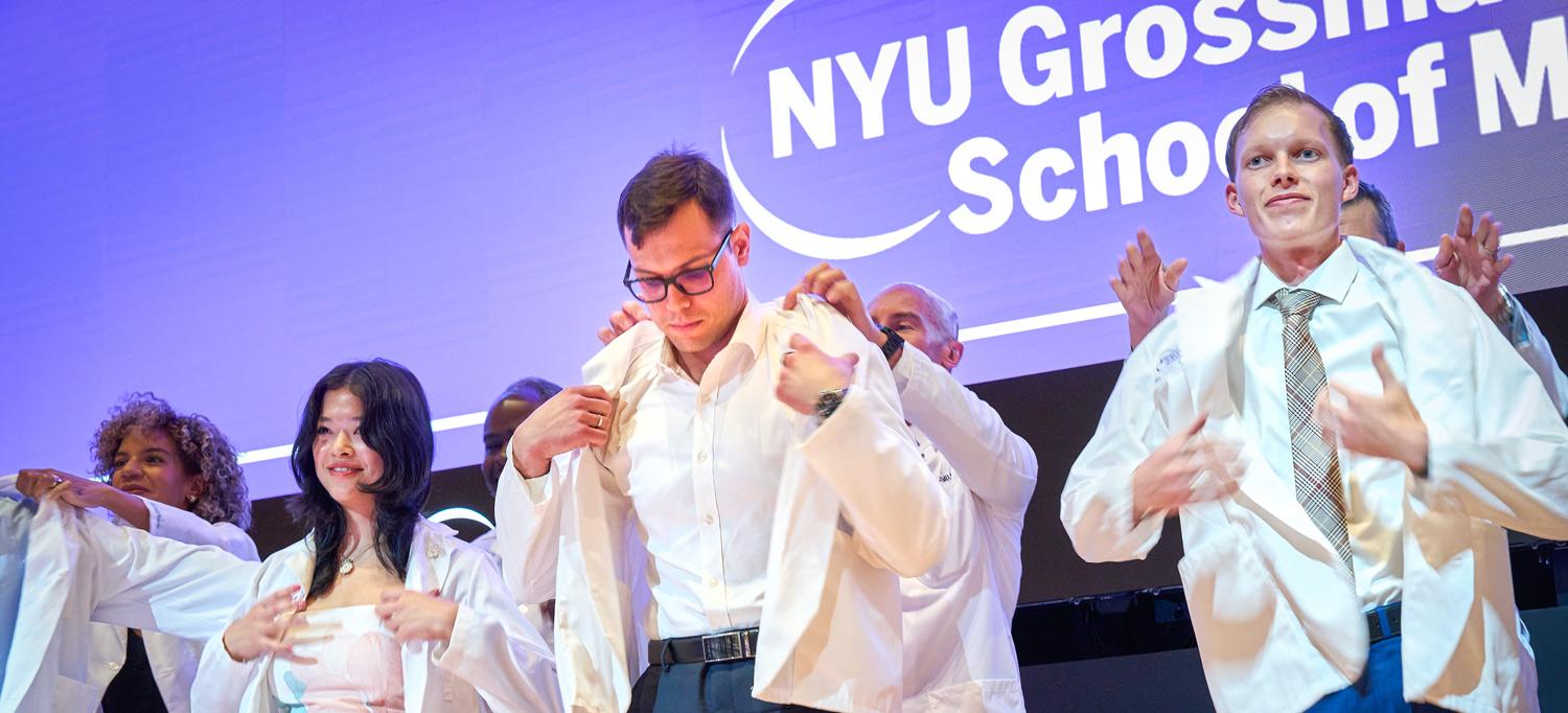 Standing on stage, four medical students put on white coats for the first time.