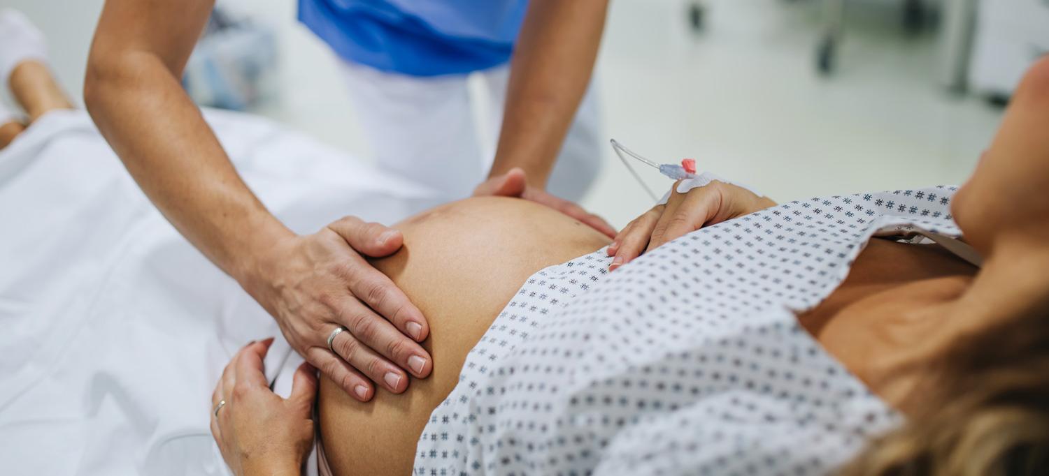 A healthcare provider places their hands on a pregnant woman’s abdomen in preparation for labor and delivery.