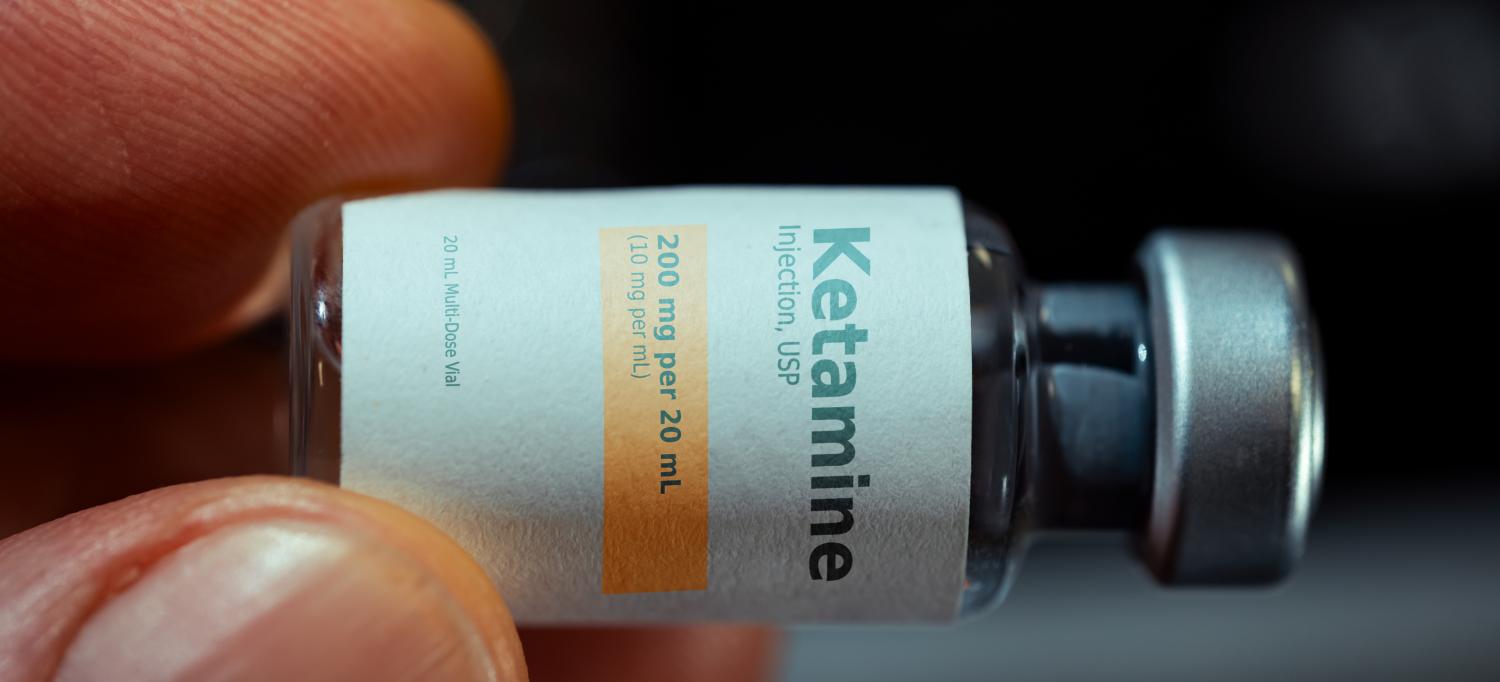 Two fingers holding a small bottle of ketamine