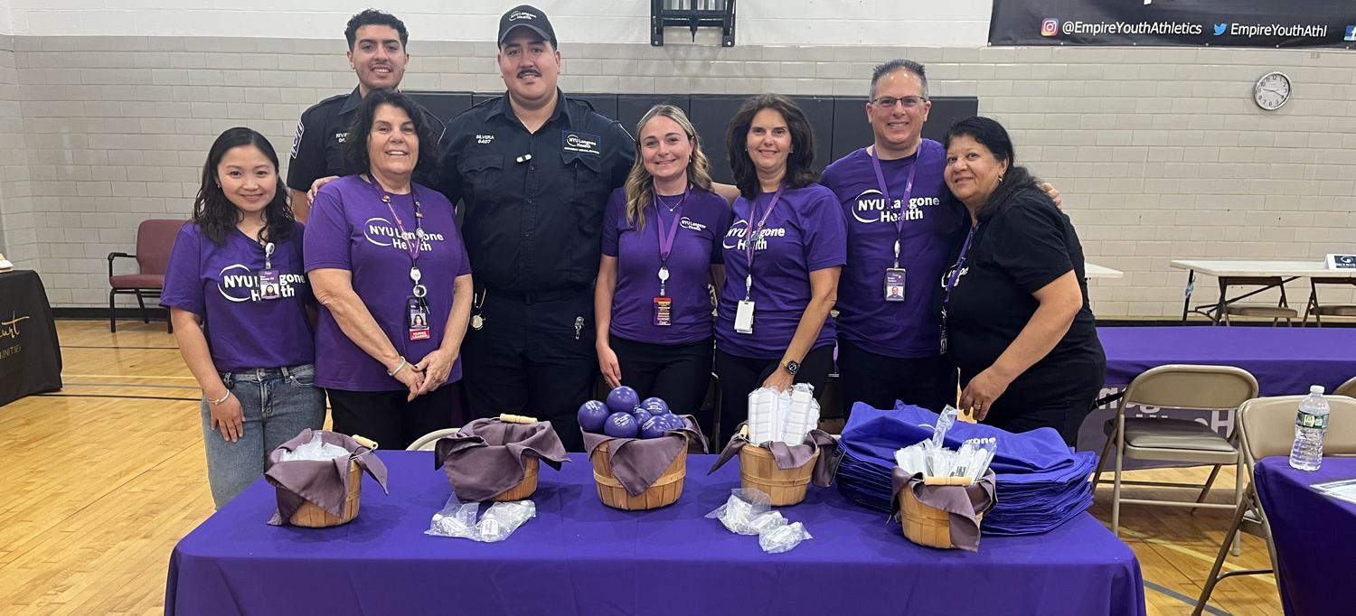 NYU Langone team members stand behind a table with a cloth that has “NYU Langone Health” written on it. 