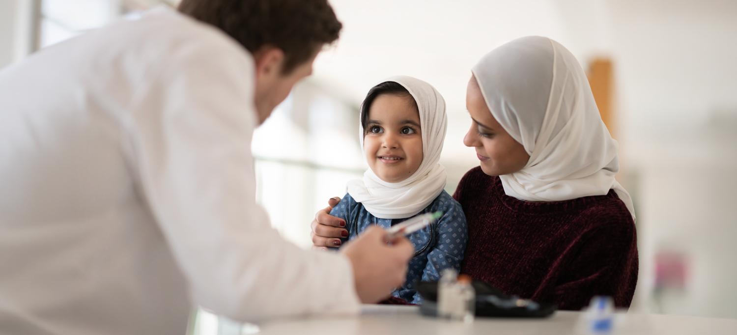 A doctor explains to a child and her mother how to inject insulin. 