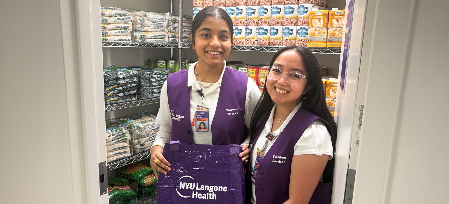Two volunteers, holding bags and smiling, stand in the food pantry.