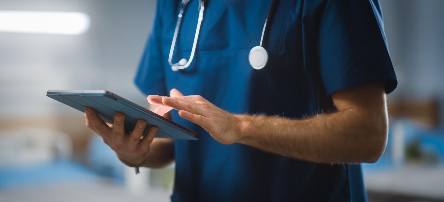 Man in scrubs entering data on an electronic tablet.