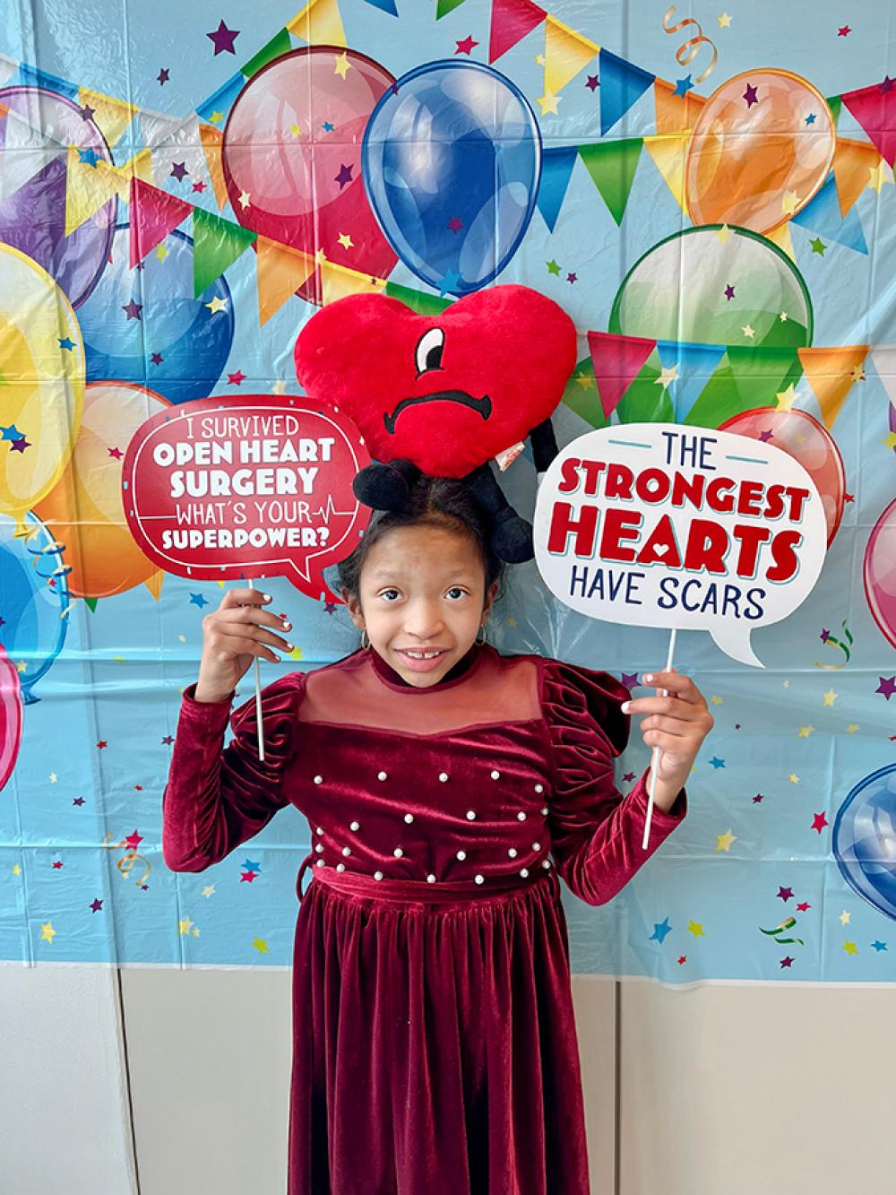 Chi Chi Holding Signs That Read I Survived Open Heart Surgery What’s Your Superpower? and The Strongest Hearts Have Scars