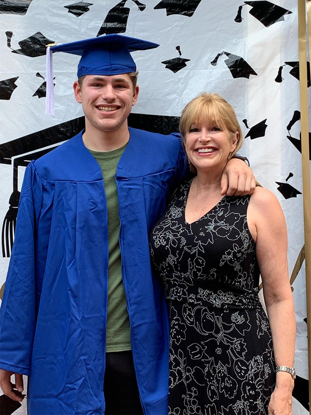 Katherine stands next to her son, who is wearing a graduation cap and gown and has his arm around her shoulders, both smiling