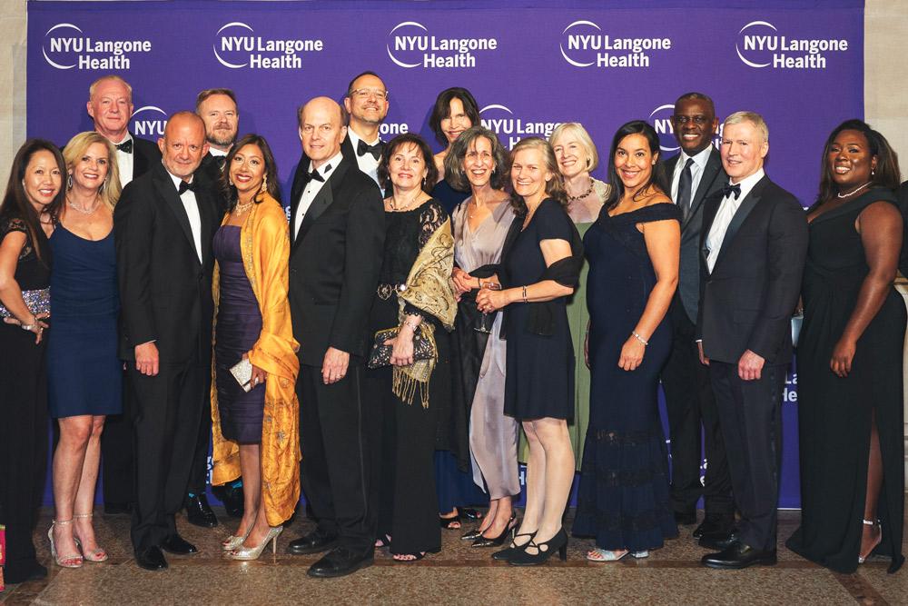 Group of people in formal wear smiling and posing in front of NYU Langone Health backdrop