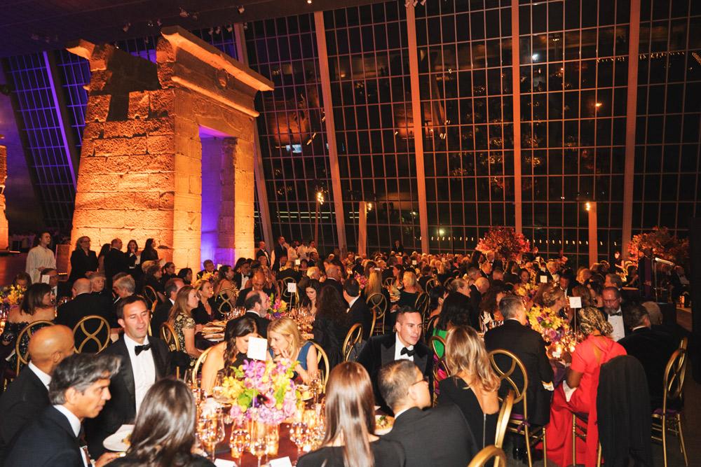 Tables full of people in formal wear drinking and eating a meal next to a stone arch