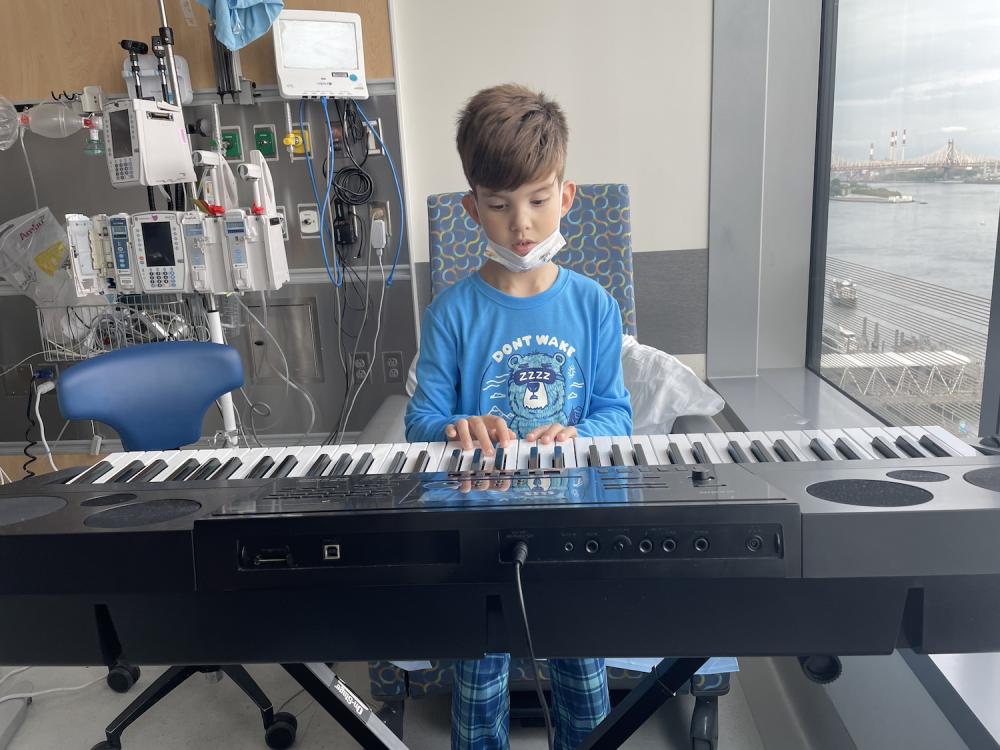 Wearing pajamas and a pulled-down face mask, Jaren plays an electronic keyboard, with medical equipment behind him.