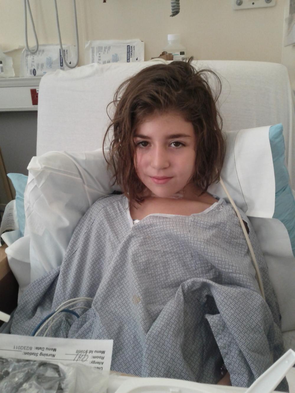 EJ wearing a hospital gown with wires attached to her, laying in a hospital bed