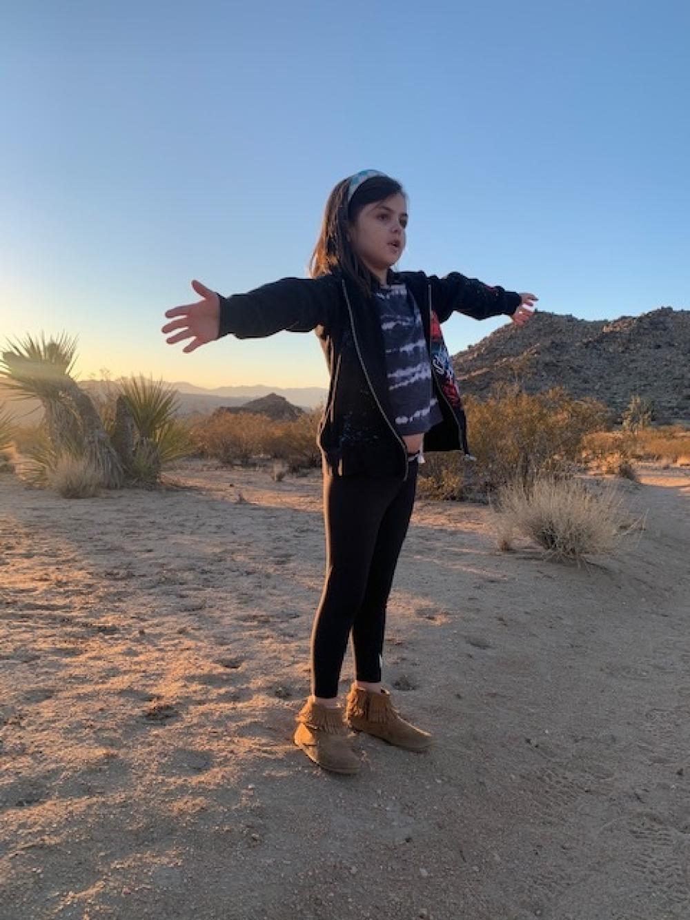 Malaya stands with her arms out in the desert.