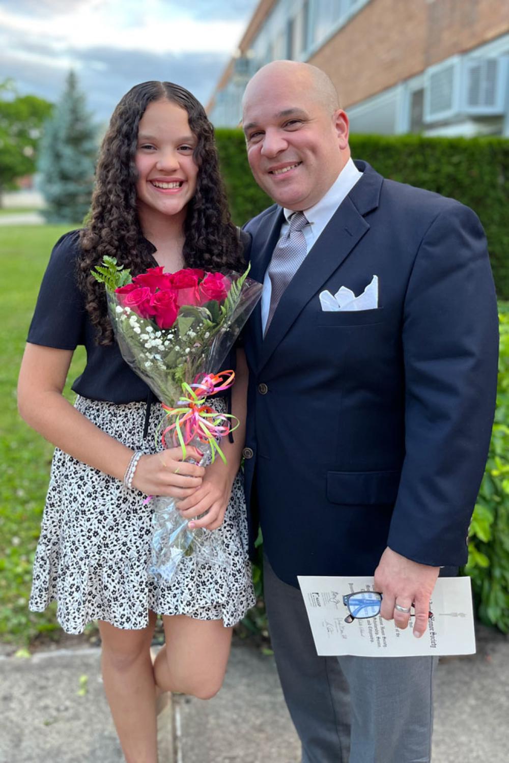 Kaitlyn holding flowers and standing next to her father, who is holding a paper from the National Honor Society