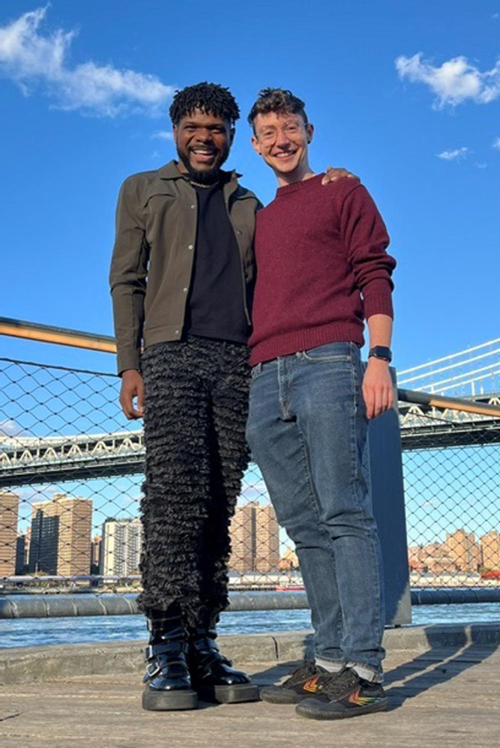 Looney and Jimenez stand together with a New York City bridge in the background.