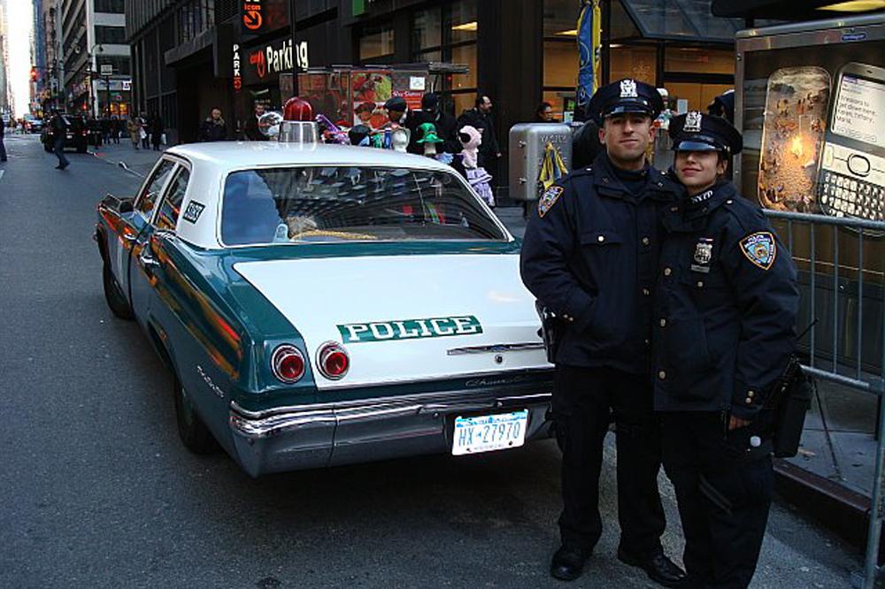 Rodriguez and his partner stand in police uniforms in front of their police car. 