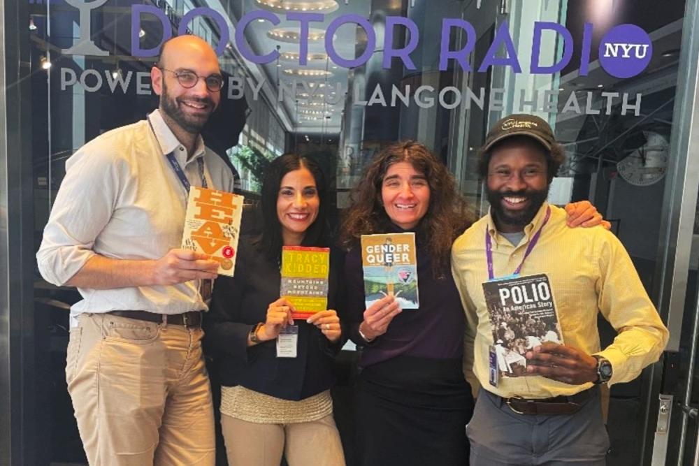 A group of NYU Langone employees stand smiling and holding copies of various book club books.