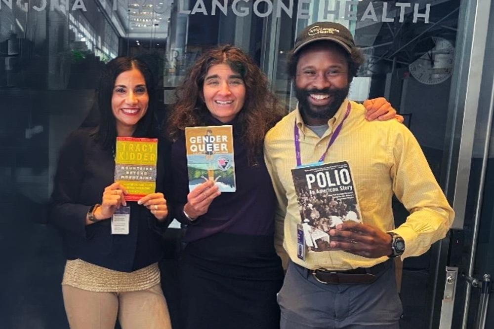 A group of NYU Langone employees stand smiling and holding copies of various book club books.