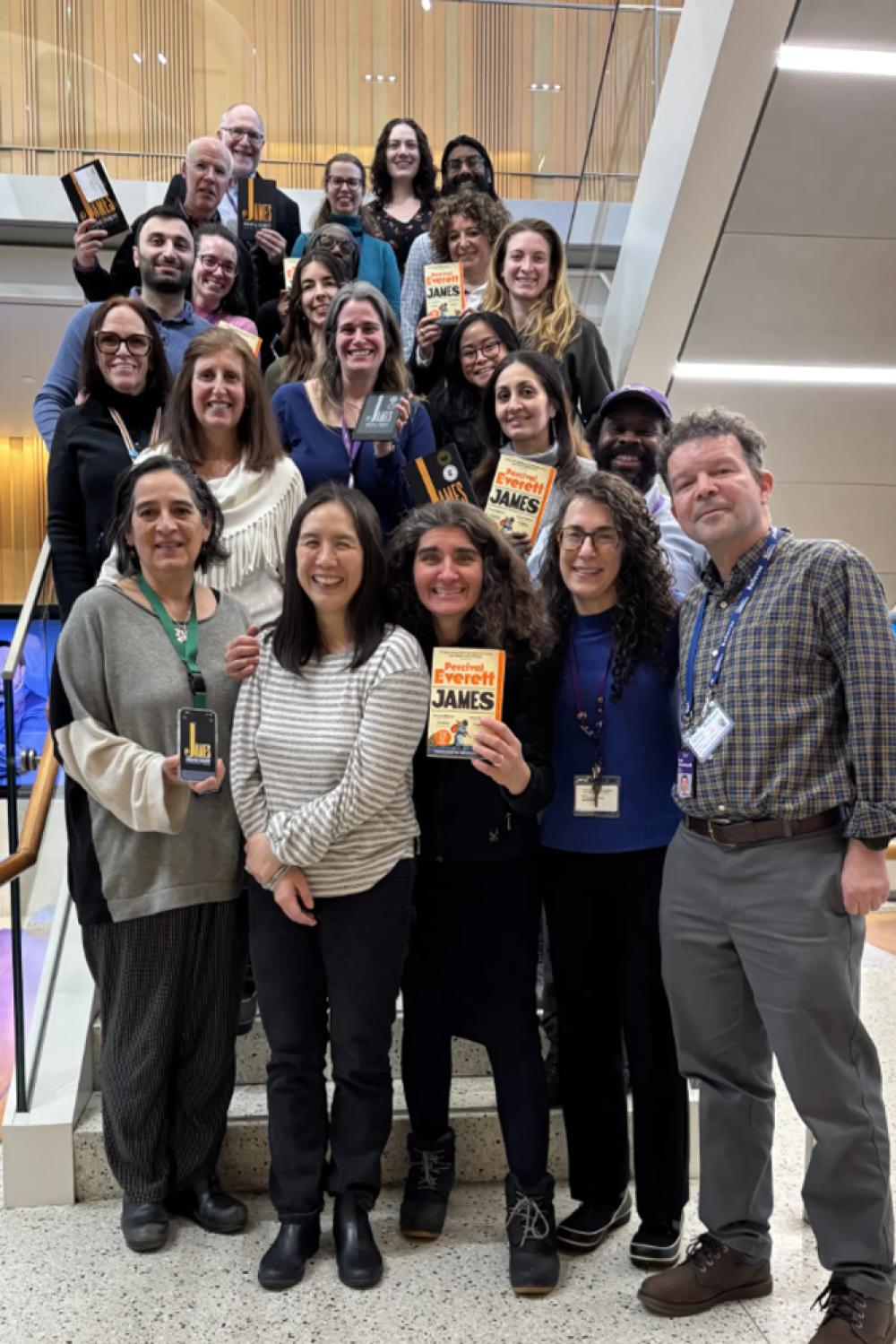 A group of NYU Langone employees stand smiling and holding a copy of the novel James, by Percival Everett.