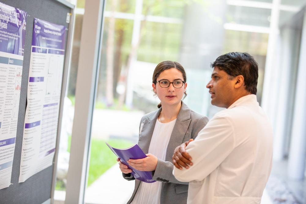 Two people discuss research in front of a poster. 
