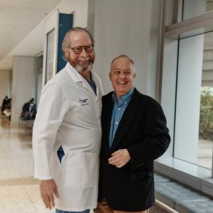 Dr. Robert Montgomery and Richard Capuano Smiling and Side Hugging in Hospital Hallway