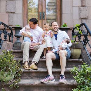 Sitting on a New York City Stoop, David Turley Kisses His 5-Month-Old Son’s Forehead While His Husband Peter Thiede Holds Their Other Son and Daughter