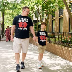 Wearing T-shirts that say “Kidney Buddies for Life,” Stephen and Jaren Munari walk together on the sidewalk.