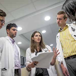 Five residents in white coats examine notes.