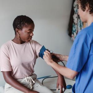 A nurse checks the blood pressure of a Black female patient in a clinic.