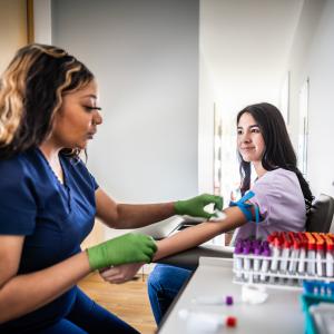 A phlebotomist prepares to draw blood from a young adult woman.