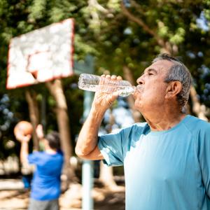 Older man drinking from a water bottle at the basketball court  