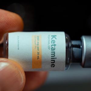 Two fingers holding a small bottle of ketamine