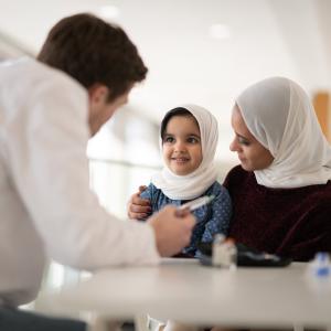 A doctor explains to a child and her mother how to inject insulin. 
