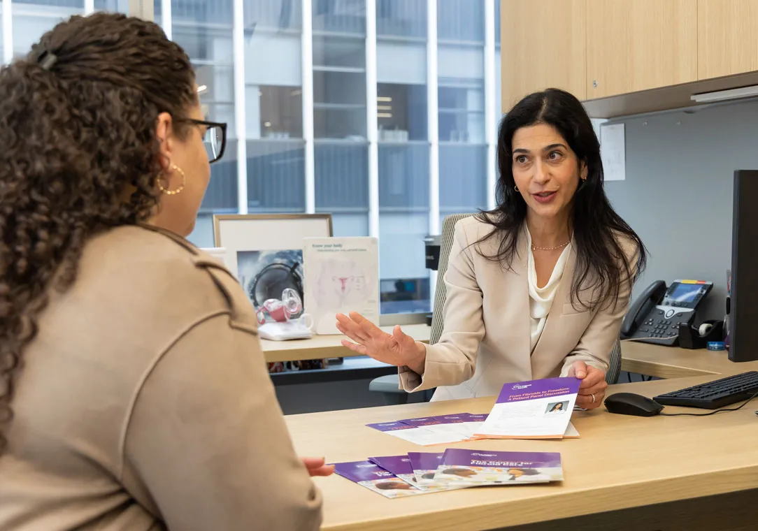 Dr. Taraneh Shirazian sits at a desk while holding a pamphlet and talking with a person across from her.