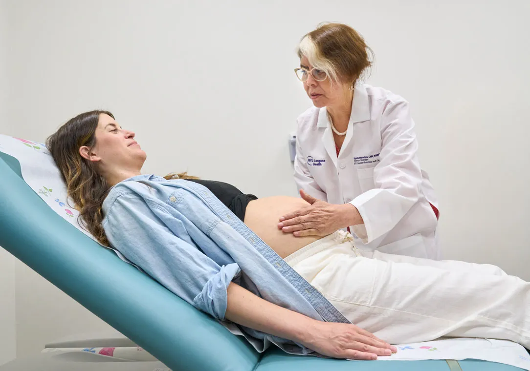 Midwife Eugenia Montesinos feels the abdomen of a pregnant woman who is lying on an exam table.