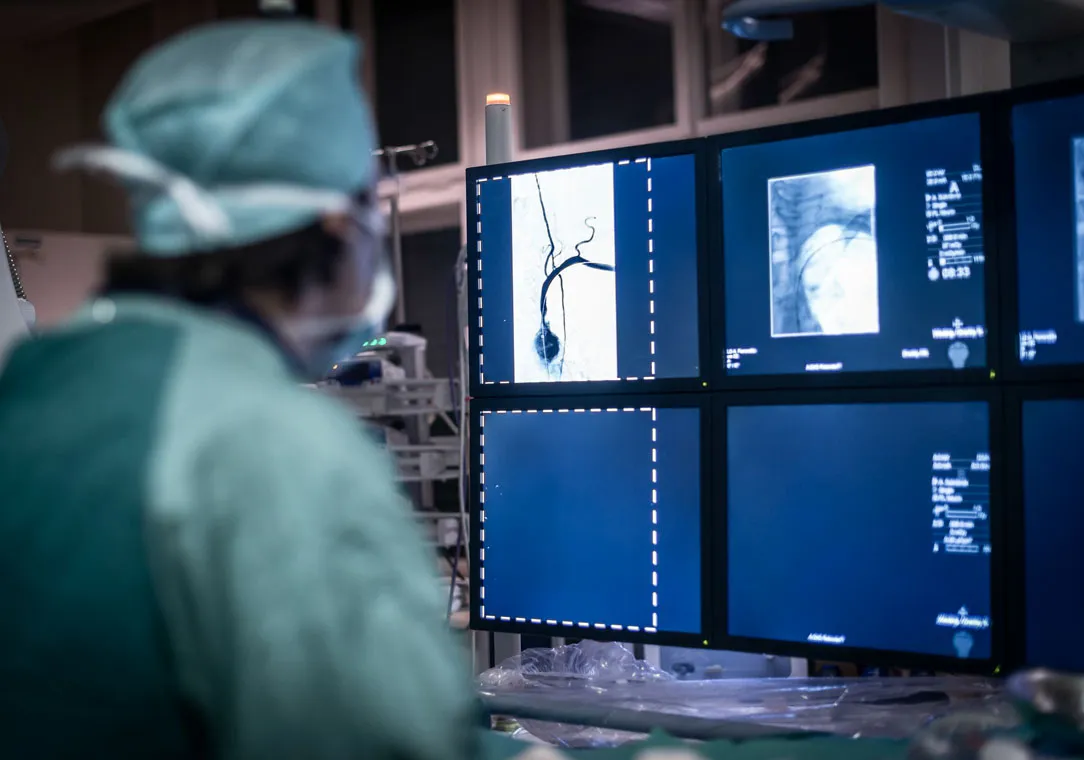 A healthcare provider in surgical scrubs observes medical imaging scans on a computer screen during a procedure.