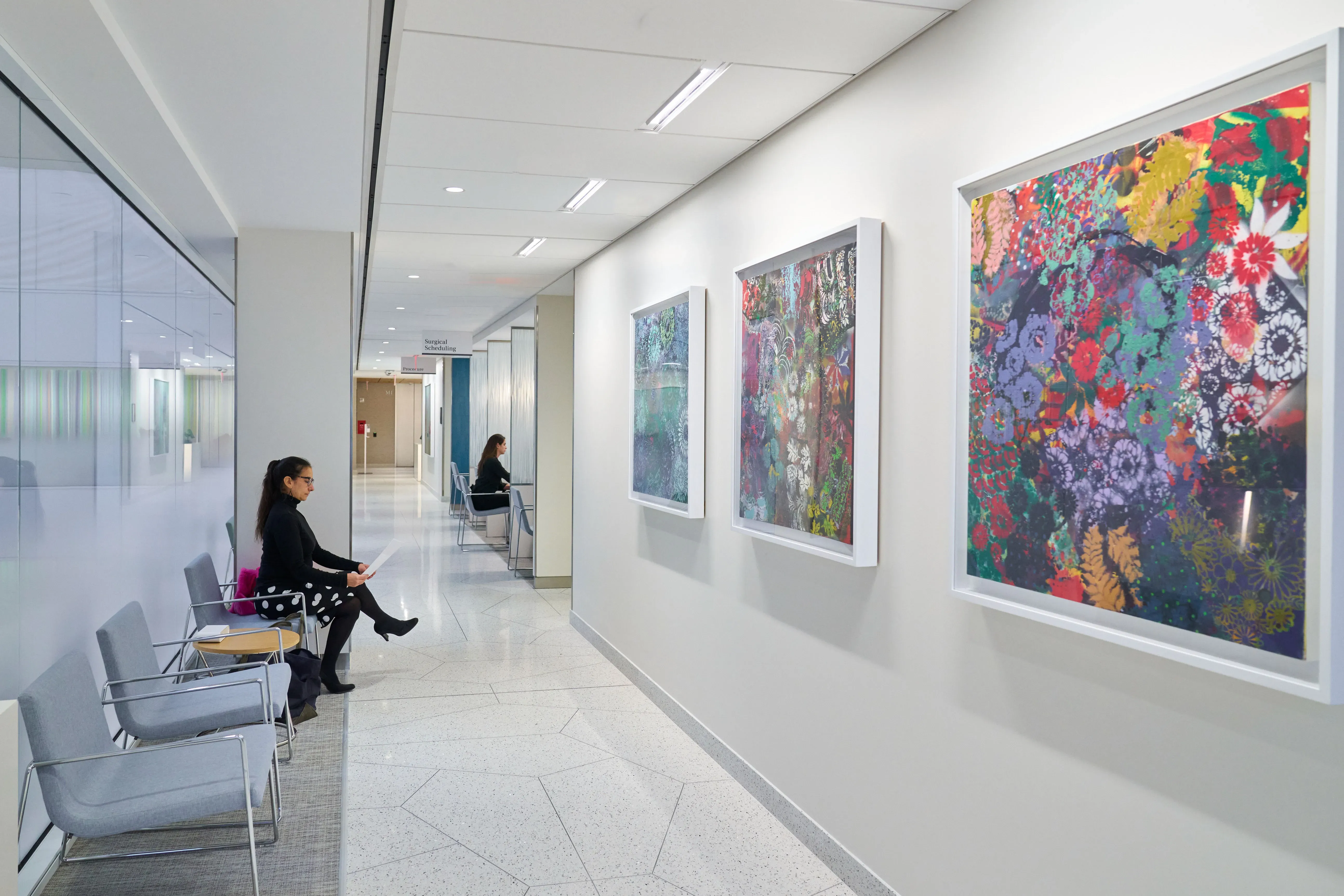 A person sits in a hallway with colorful floral artworks displayed on the walls.