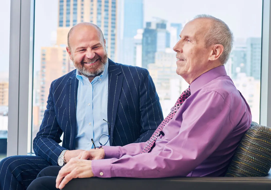 Dr. Samer Al-Homsi sits smiling in a blue suit as he talks to a patient in a purple shirt.