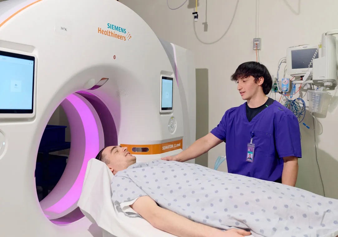 A healthcare worker prepares a patient for a CT scan inside a hospital imaging room.